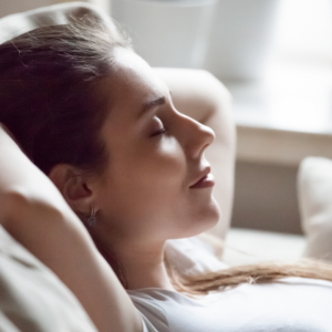 Frau liegt mit geschlossenen Augen im Bett. Suggeriert eine erotische Hypnose.