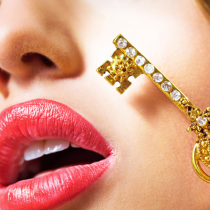 Ausschnitt eines weiblichen Gesichts. Die Lippen, rot-rosa geschminkt und leicht geöffnet. Ein goldener Schlüssel liegt leicht an der Wange an.
